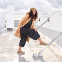Model wearing Bearpaw Calista clogs in a neutral tone, styled with a camel coat and dark denim in an outdoor rooftop setting.
