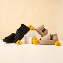 Bearpaw platform sandals in black and beige displayed on a minimal set with yellow flowers, highlighting summer style and comfort
